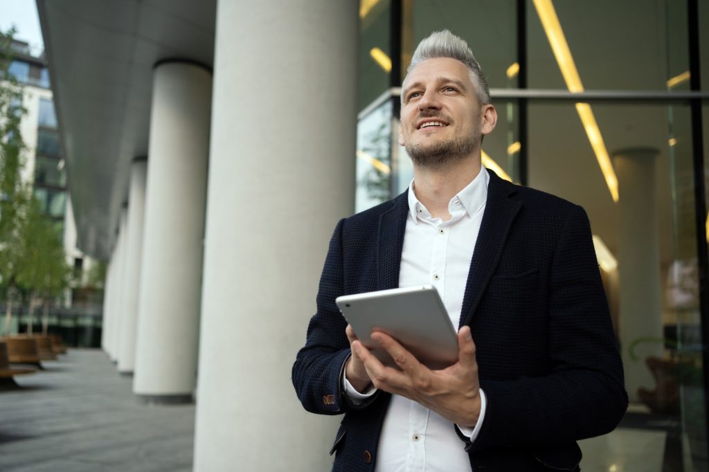 Optimistic businessman with a tablet looking up, inspired by the urban landscape.